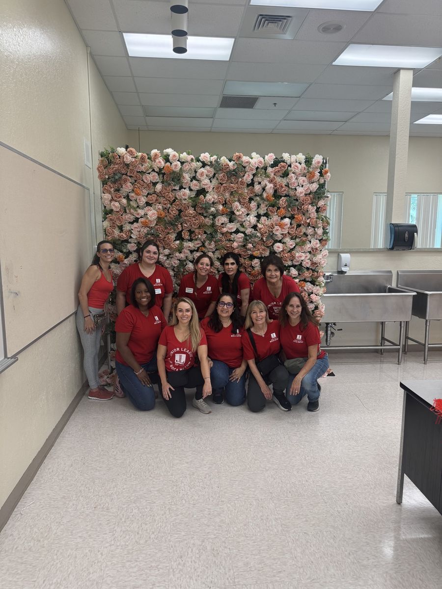 Brittanny with Junior League of Boca Raton members in red shirts in front of a flower wall